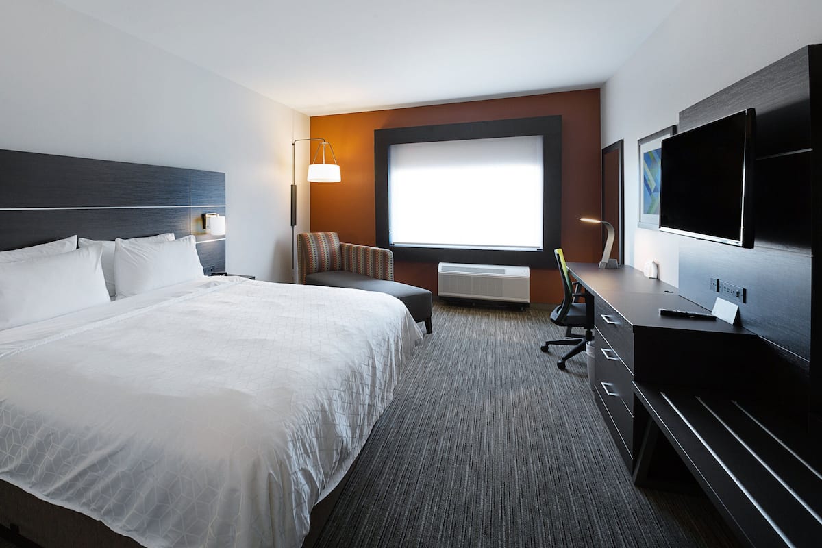 Habitación de hotel con una cama grande, un escritorio con computadora, un televisor y una ventana con vistas.
