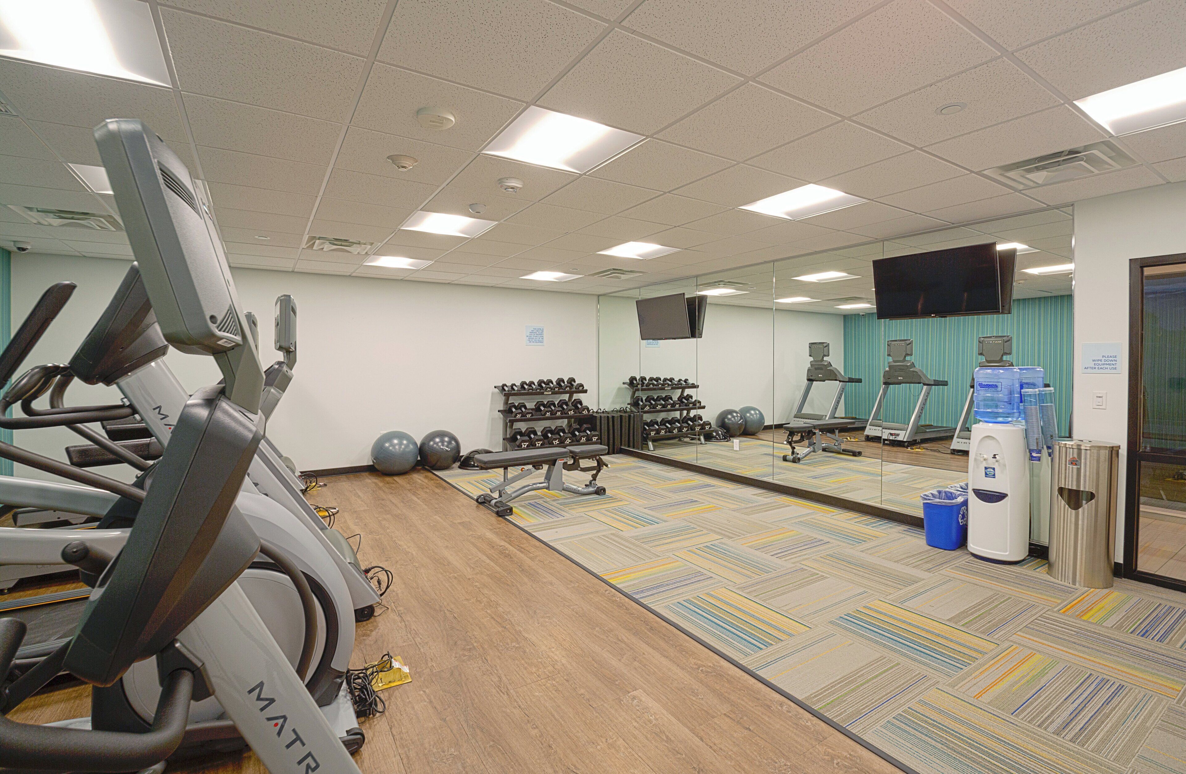 A gym with treadmills, dumbbells, exercise balls, and a mirror wall.