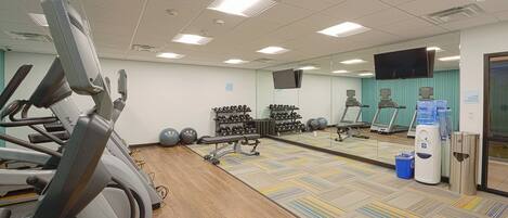 A gym with treadmills, dumbbells, exercise balls, and a mirror wall.