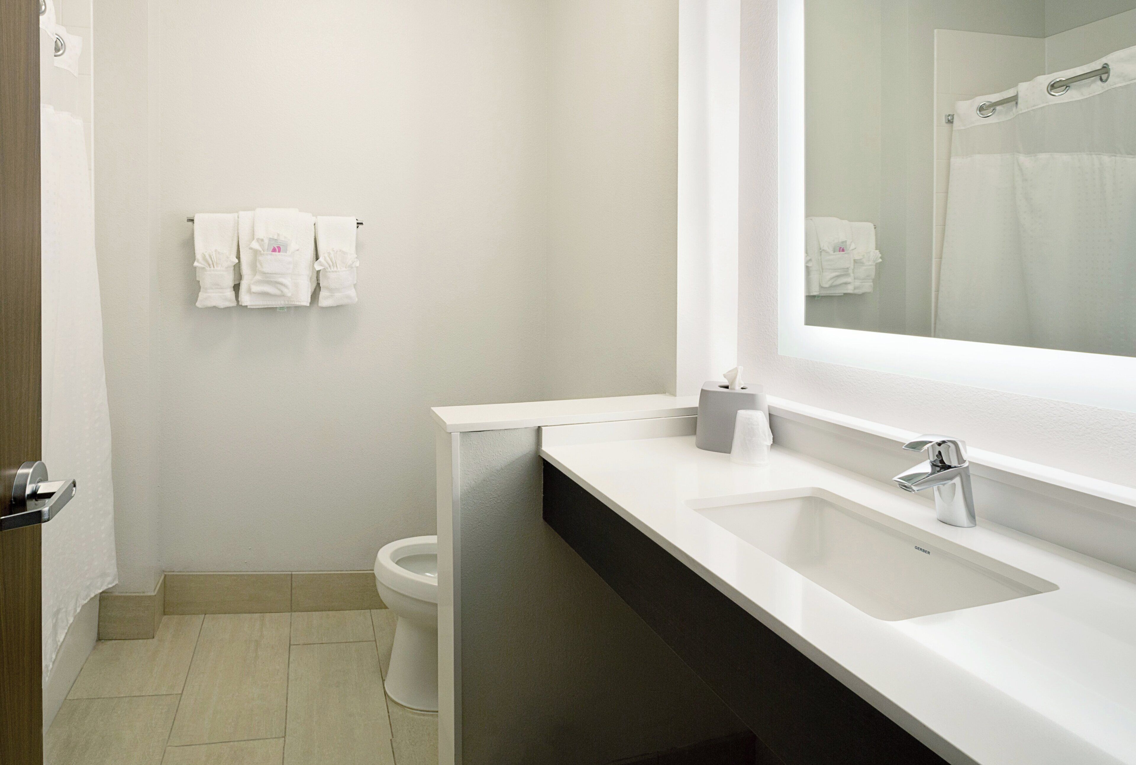Un bagno con il water, un lavandino, uno specchio e un portasciugamani con asciugamani.