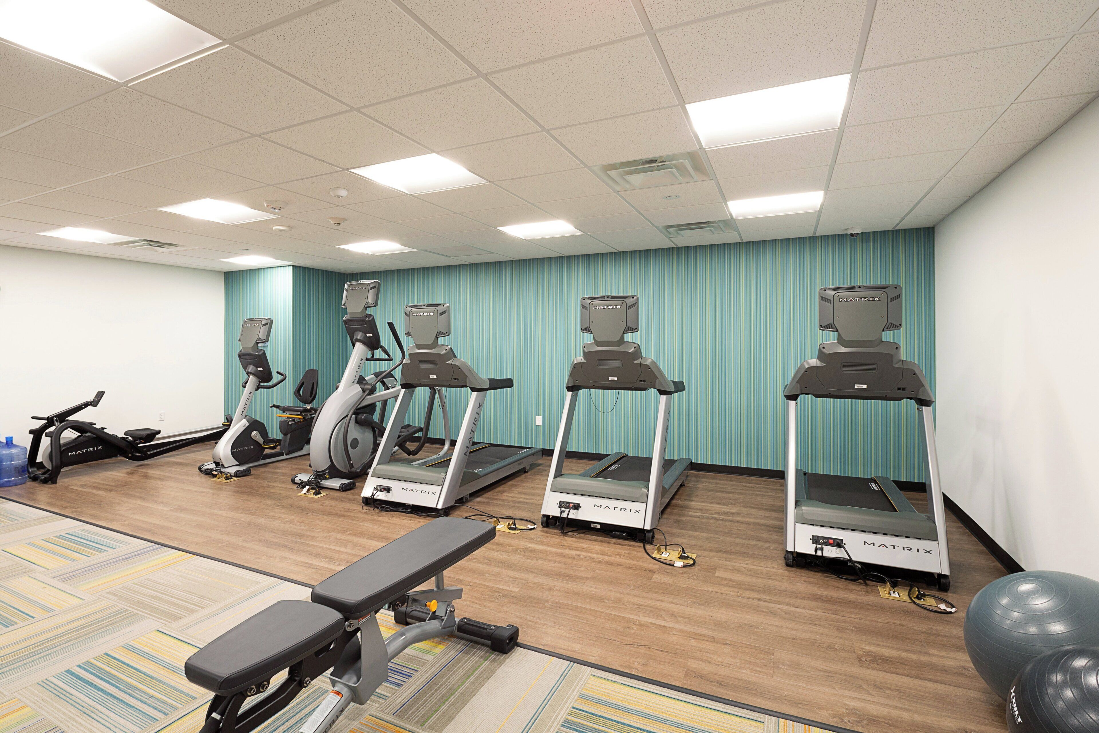 A fitness room with treadmills, a stationary bike, and a bench.