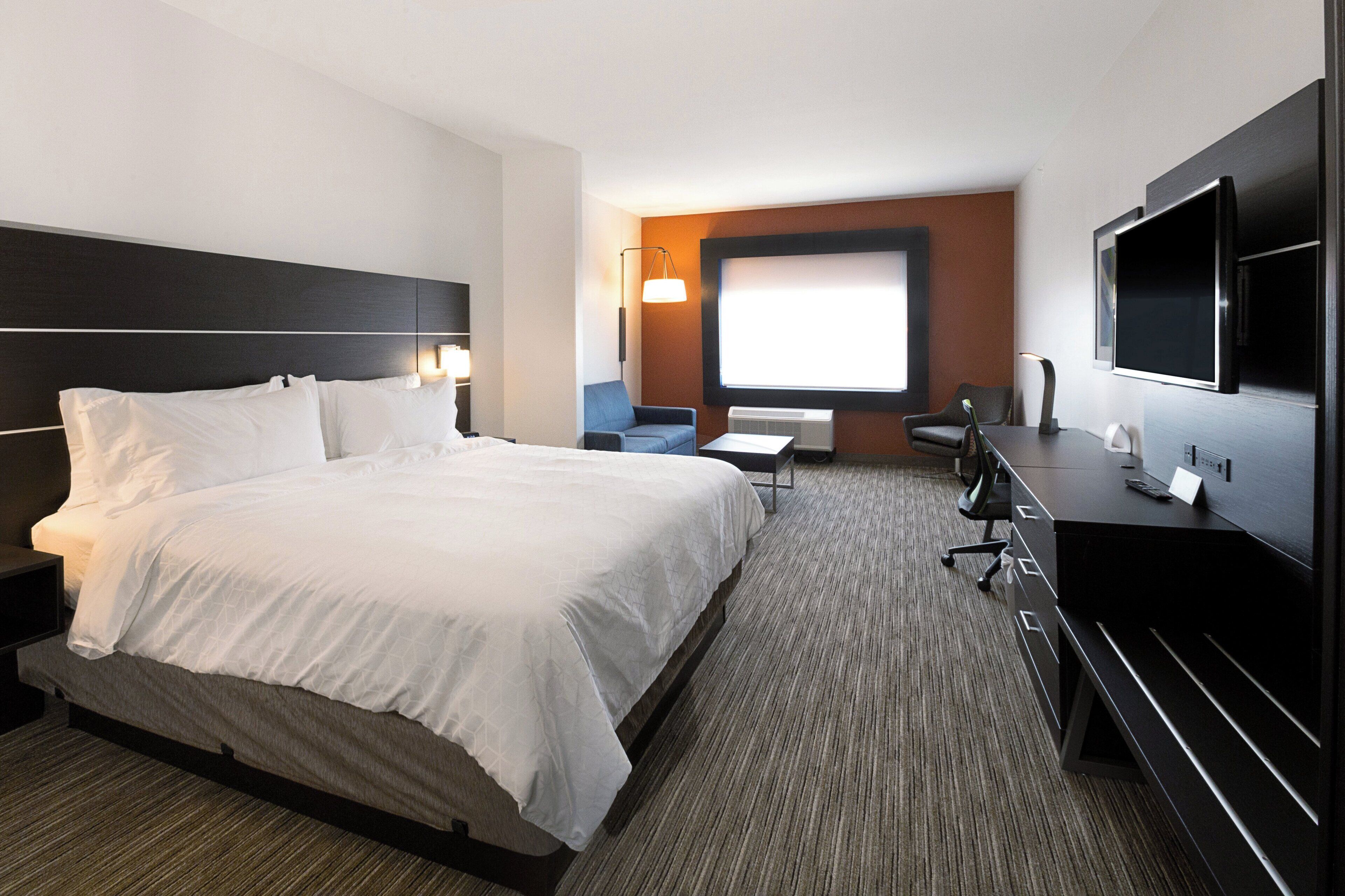 A hotel room with a large bed, a desk, a chair, a TV, and a window.