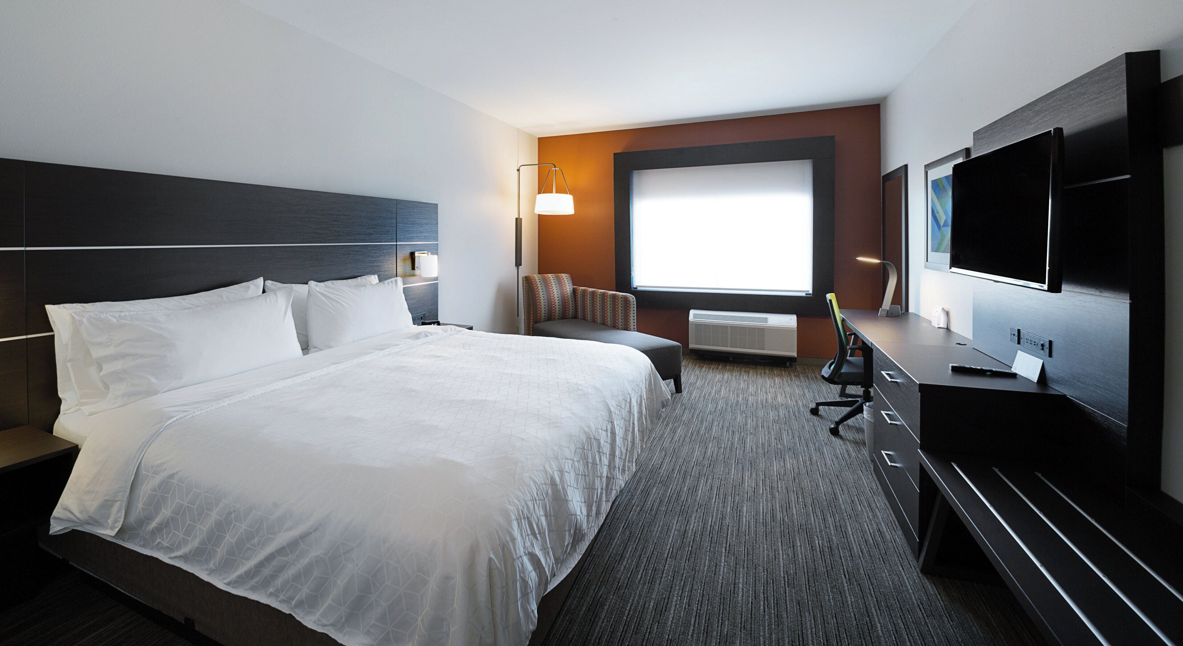 Habitación de hotel con una cama grande, un escritorio con computadora, un televisor y una ventana con vistas.