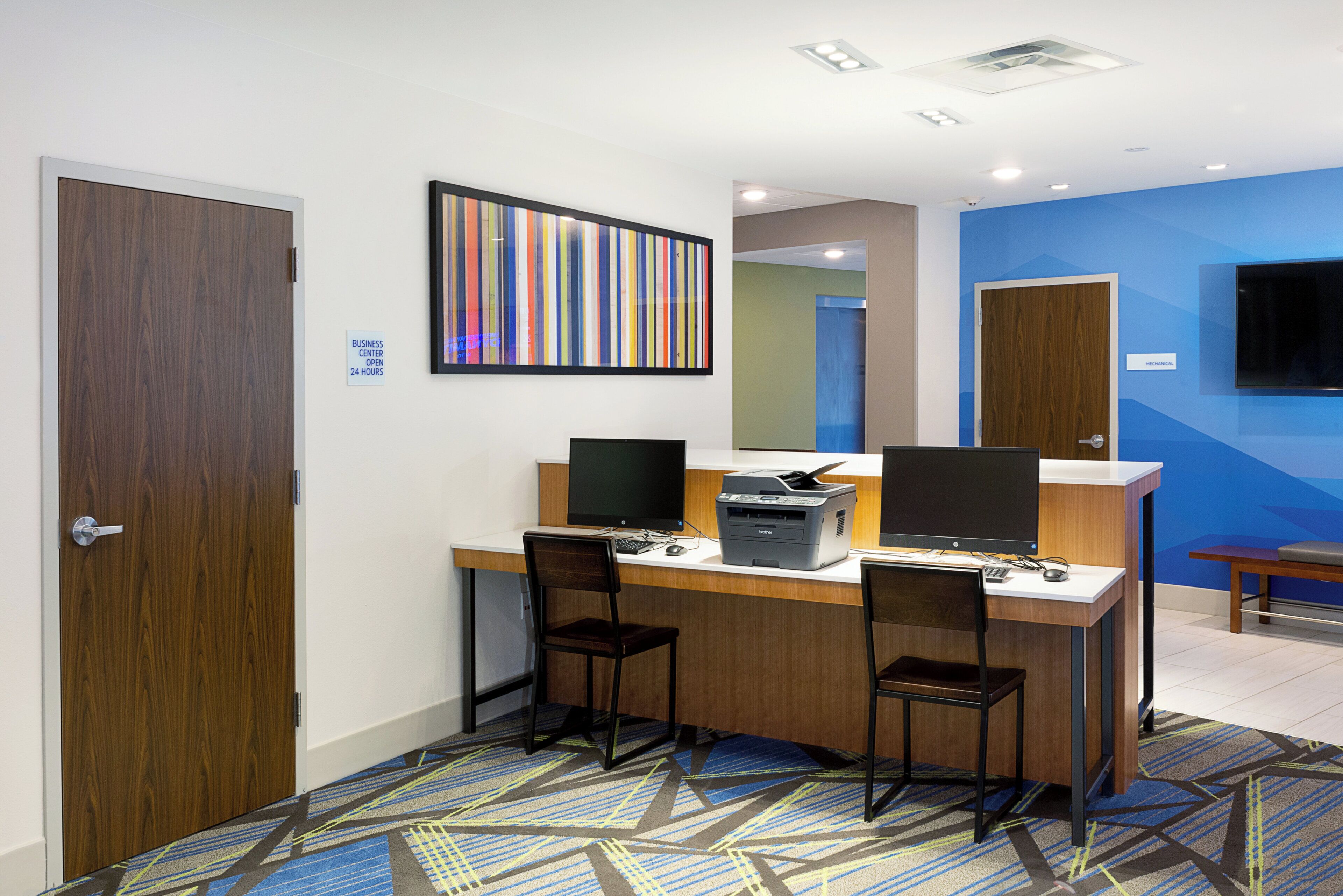 A hotel business center with two computer workstations, chairs, and a printer.