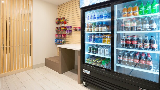 Máquina expendedora con diversas bebidas y aperitivos, una puerta de listones de madera y una barra blanca.