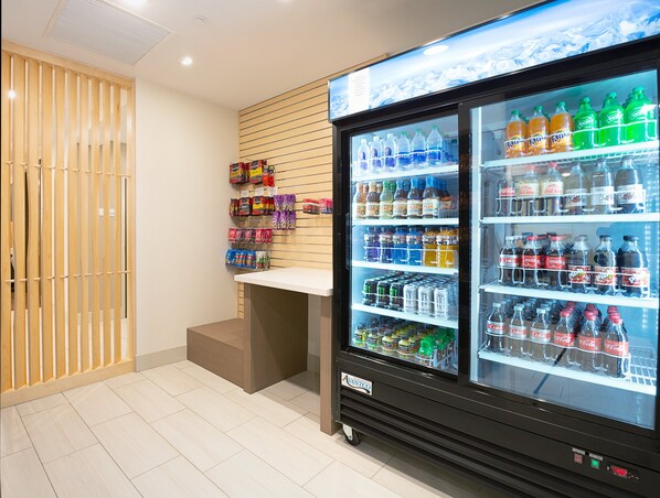 Een automaat gevuld met verschillende drankjes en snacks, een deur van houten latten en een witte toonbank.