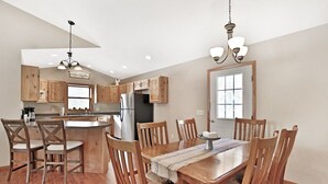 A modern kitchen with wooden cabinets, a stainless steel refrigerator, and a dining area with a wooden table and chairs. - Elroy's @ Big Rock Creek: Where Adventure Meets Comfort in the St. Croix Valley (Saint Croix Falls)