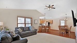 A spacious living room with a grey sofa, a dining area with wooden chairs, and a kitchen in the background. - Elroy's @ Big Rock Creek: Where Adventure Meets Comfort in the St. Croix Valley (Saint Croix Falls)