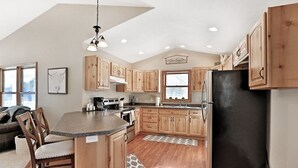 A kitchen with wooden cabinets, a black refrigerator, and a dining area with a chair and a rug. - Elroy's @ Big Rock Creek: Where Adventure Meets Comfort in the St. Croix Valley (Saint Croix Falls)