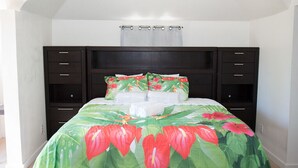 A bed with a floral bedspread, a dark headboard, and a white curtain. - COCOPLUM REST N HIDEAWAY #2 (Bahamas)