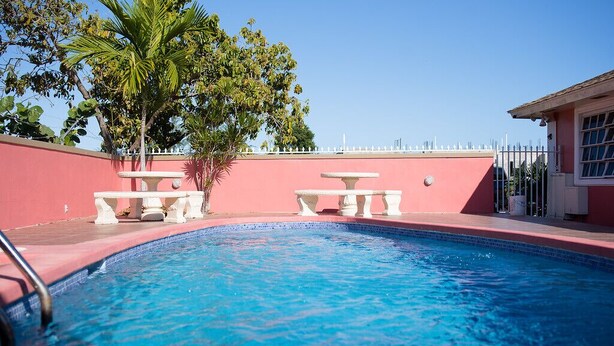 A swimming pool with two white tables and chairs, surrounded by a pink wall and a white fence. - COCOPLUM REST N HIDEAWAY #2 (Bahamas)
