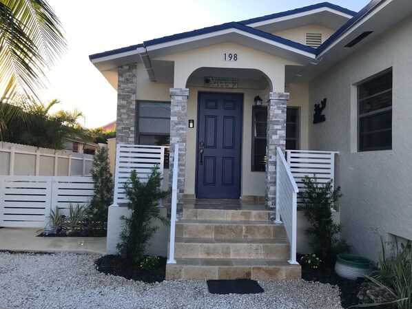 Uma casa com porta azul, número 198, e um pequeno alpendre com degraus que levam à entrada.