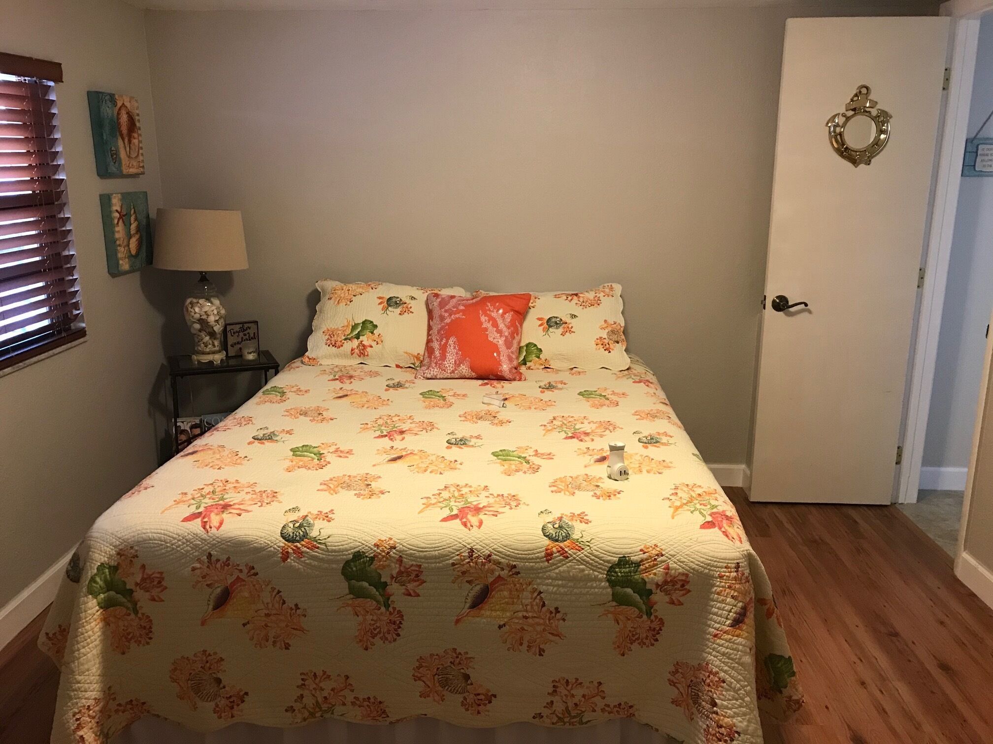 A bedroom with a floral bedspread, a nightstand with a lamp, and a door with a decorative handle.