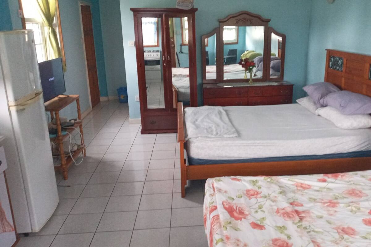 Ein Schlafzimmer mit einem Holzbett, einem Schminktisch mit Spiegel, einem Kühlschrank und einem Fenster mit Vorhängen.