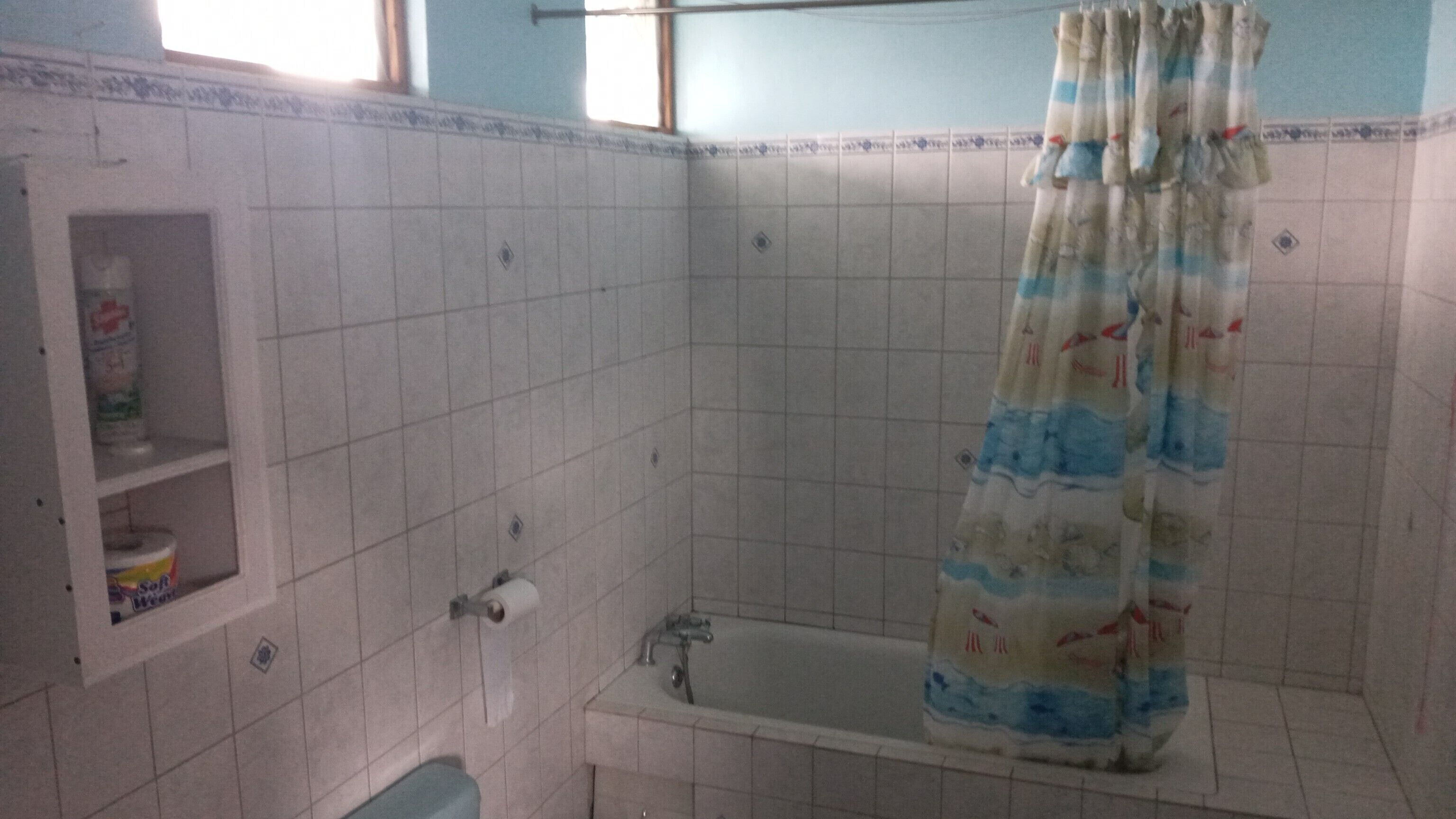 Et badeværelse med badekar, bruseforhæng og en hylde med toiletartikler.