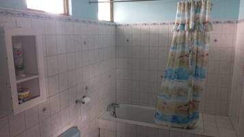 Et badeværelse med badekar, bruseforhæng og en hylde med toiletartikler.