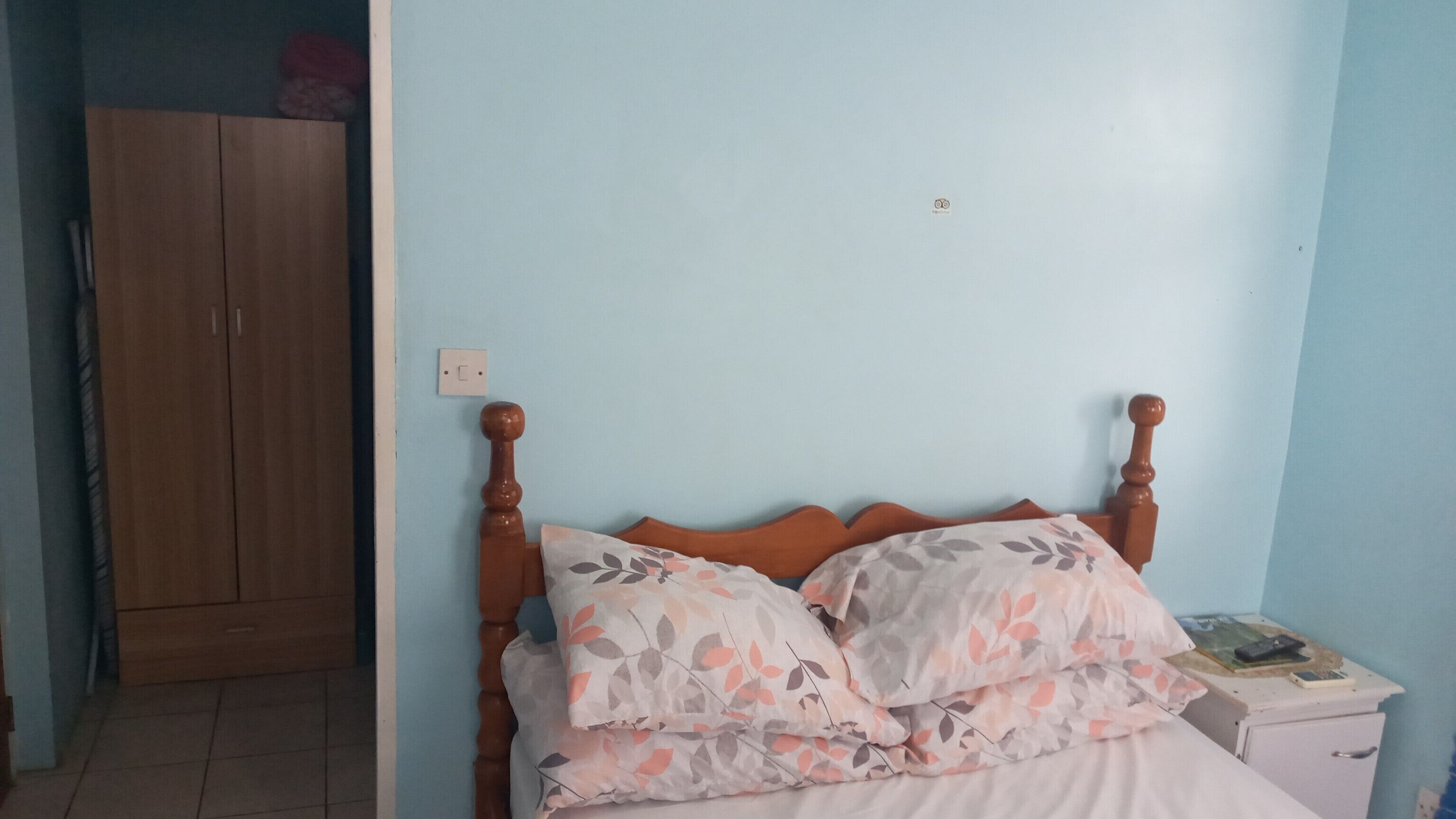 Une chambre à coucher avec un lit en bois, une literie à motifs floraux, une table de chevet, une petite armoire blanche et une garde-robe.