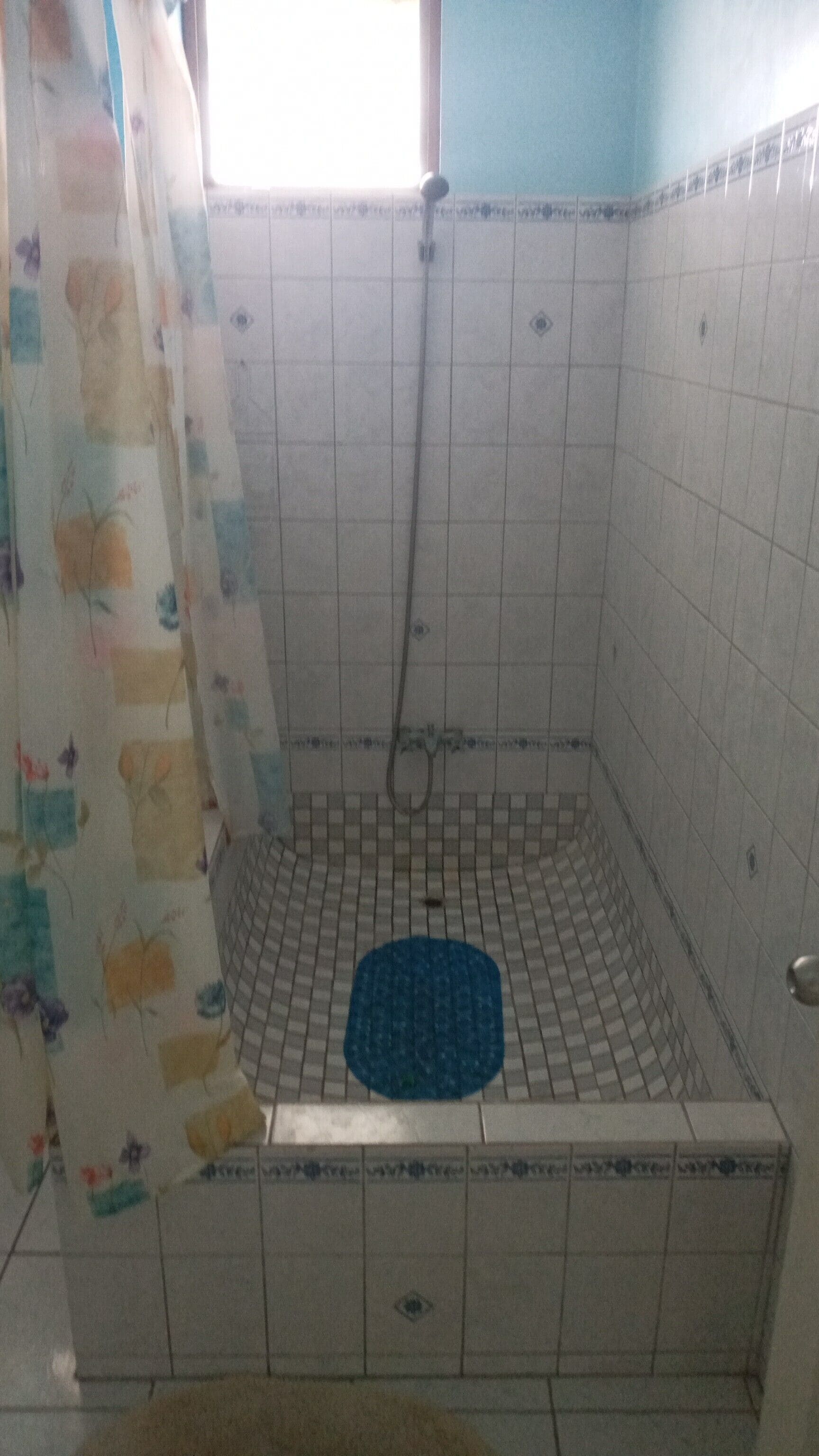 Un espacio de ducha pequeño, con azulejos, una cortina de ducha y una alfombra azul.