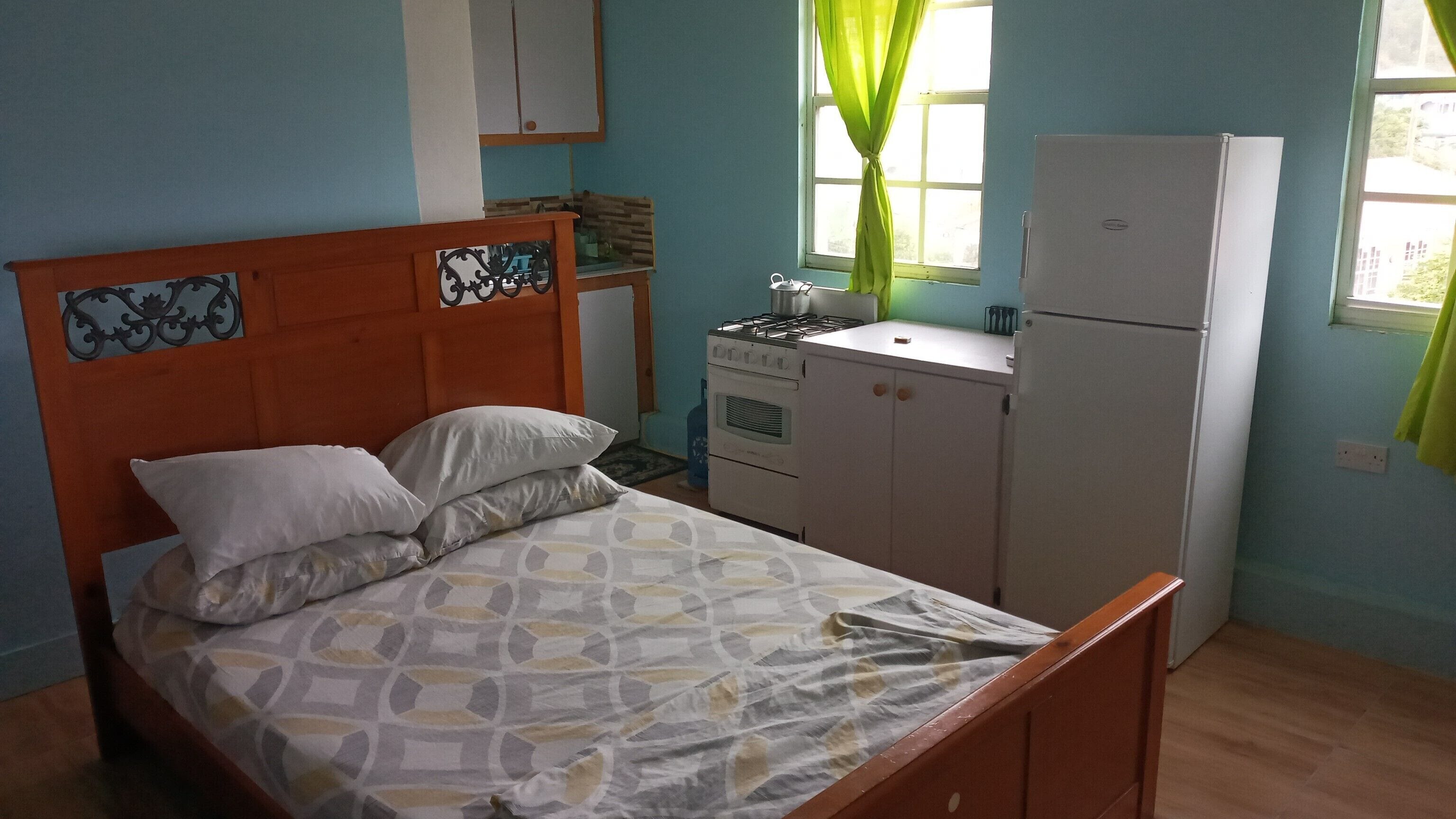 Une chambre avec un lit, une petite kitchenette équipée d’une cuisinière et d’un réfrigérateur, et une fenêtre avec des rideaux.