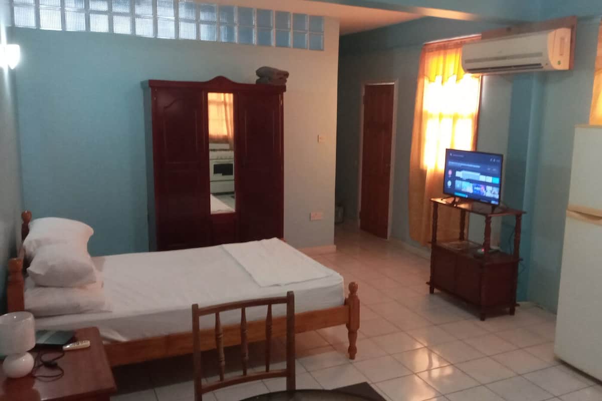 Ein kleines, sauberes Zimmer mit einem Bett, einem Schreibtisch, einem Stuhl, einem Fernseher und einem Kühlschrank.