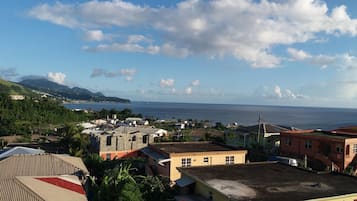 A coastal town with buildings, a view of the sea, and a hilly landscape in the background.