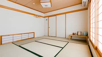 A tatami mat room with a sliding door, a small table with a cup, and a heater on the wall.