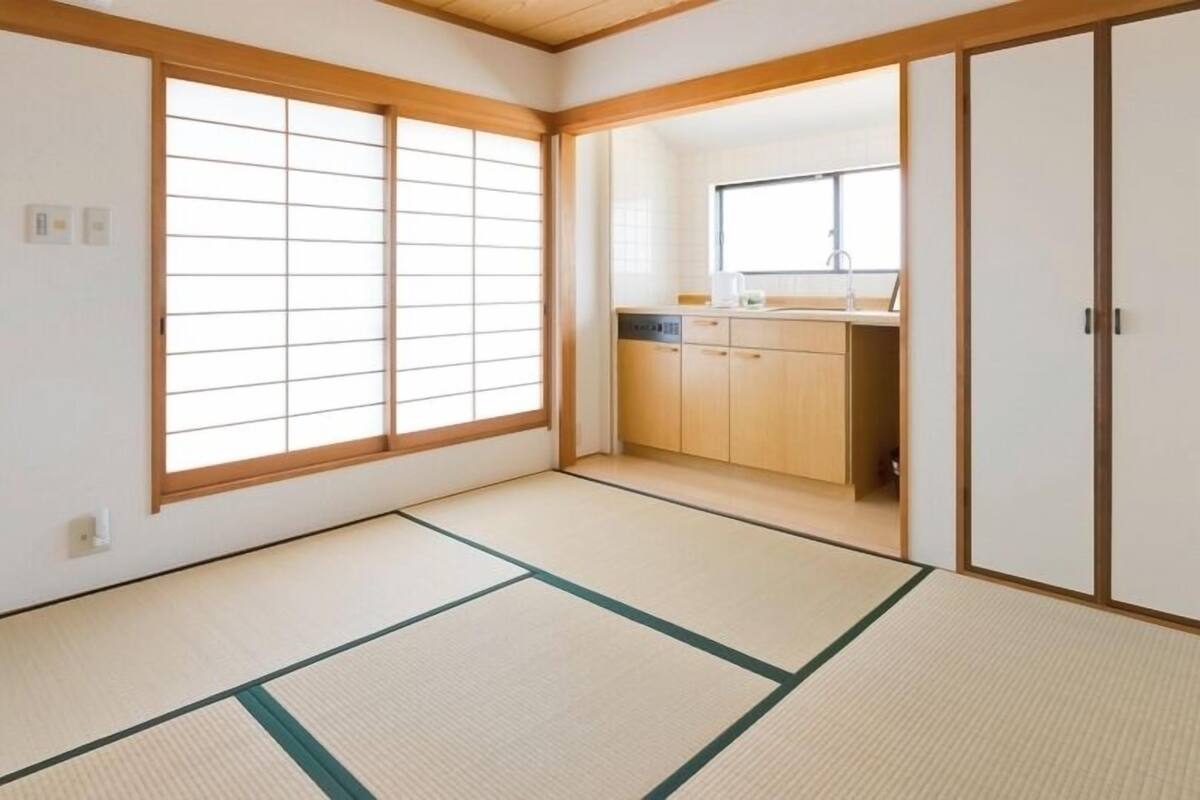A room with tatami flooring, a sliding door, and a view of a kitchen area.