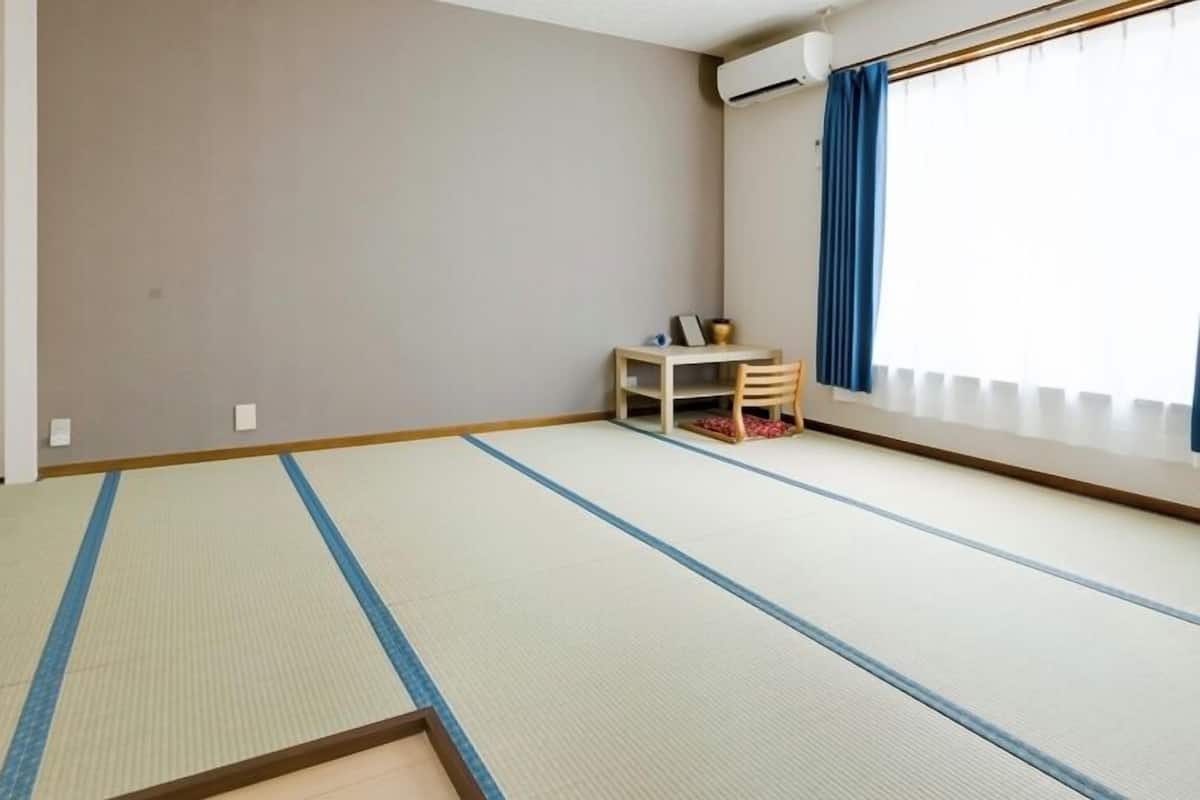 A room with tatami mat flooring, a small table with a chair, and a window with curtains.