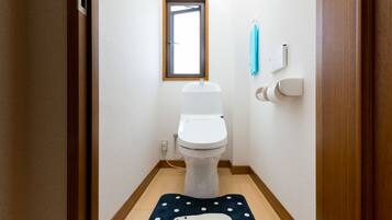 Une petite salle de bain propre, avec des toilettes, une fenêtre et un tapis bleu orné d’un motif d’ours polaire.