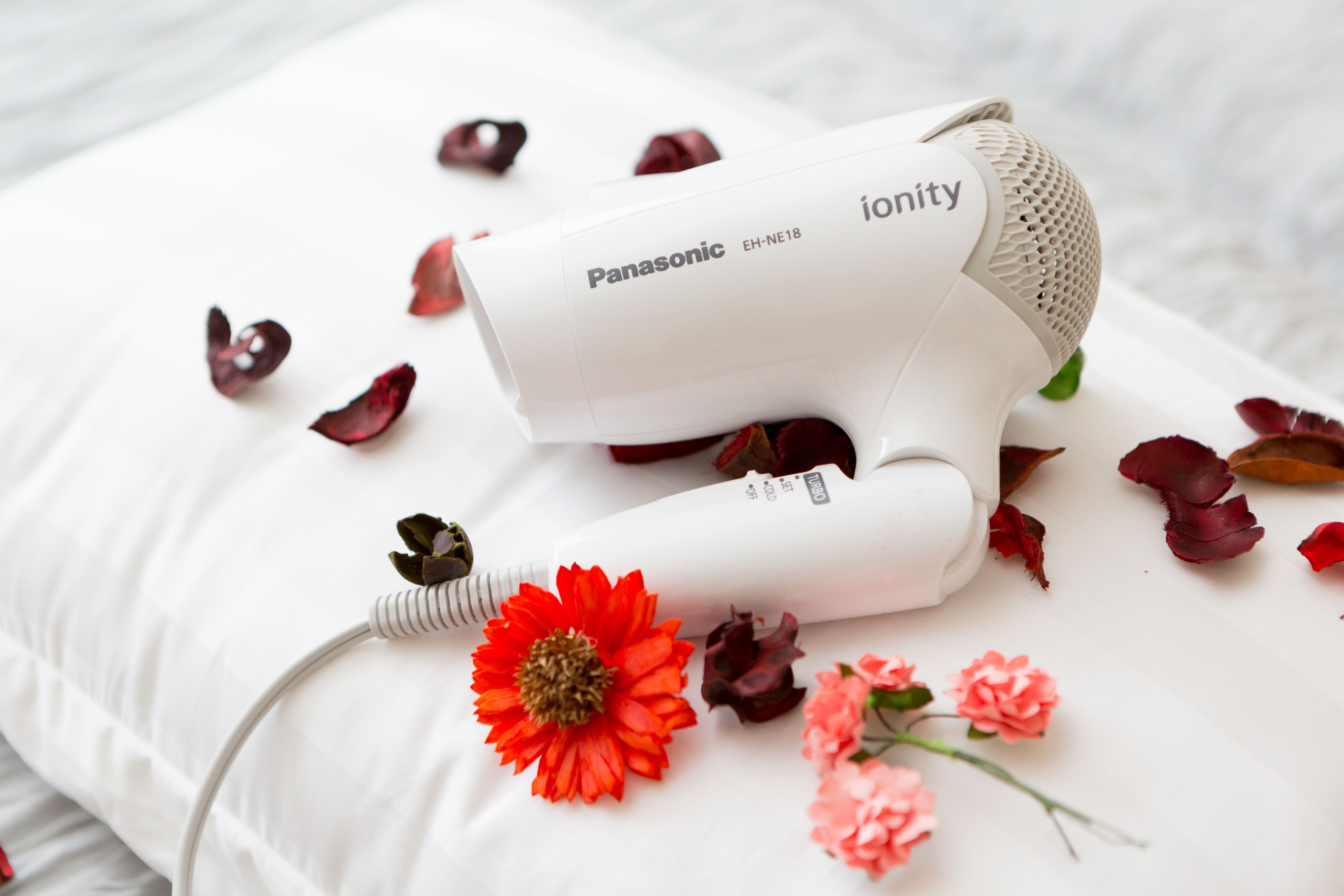 Een Panasonic haardroger op een wit kussen, omringd door rode en roze bloemen.