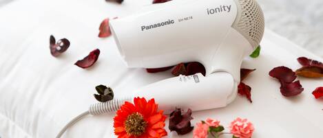 Een Panasonic haardroger op een wit kussen, omringd door rode en roze bloemen.