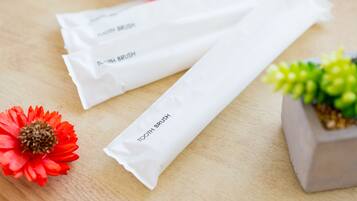 Three white toothbrush packages labeled "TOOTH BRUSH" on a wooden surface with a red flower and a small potted plant.