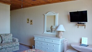 Une chambre à coucher comprenant un lit, une commode, une chaise, un bureau, un téléviseur et un ventilateur de plafond.