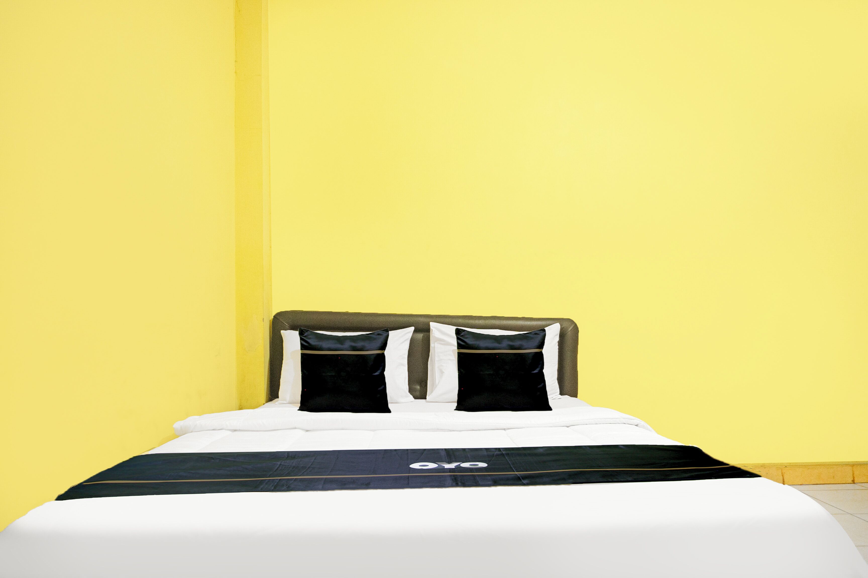 A bed with a black and white bedspread, two black pillows, and a headboard against a yellow wall.