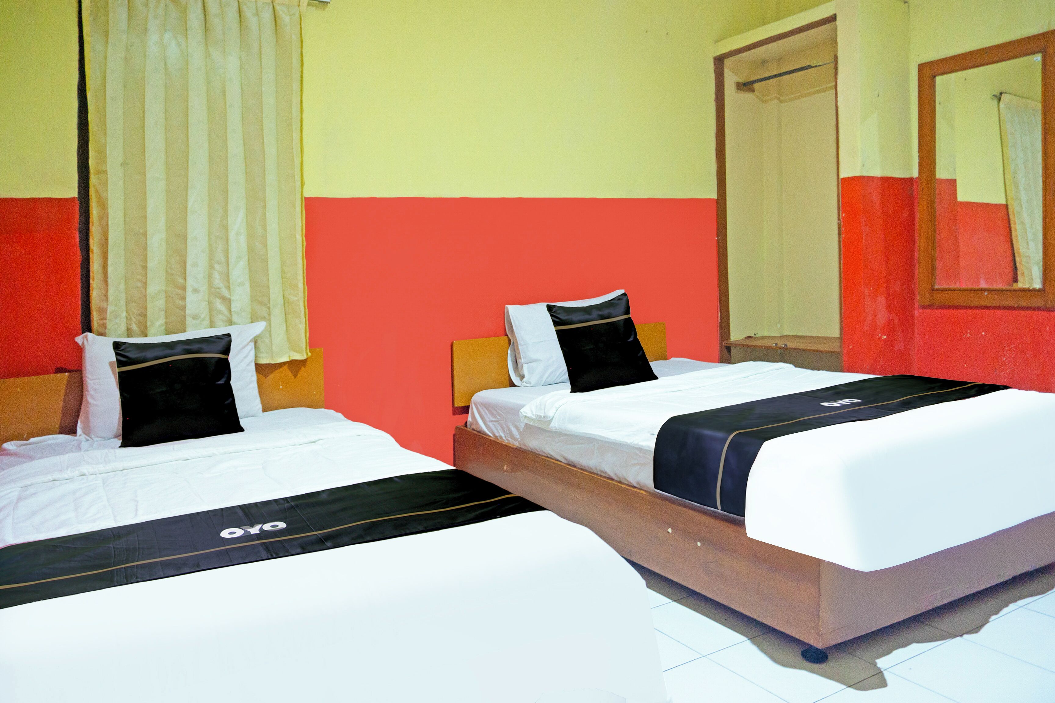 A hotel room with two beds, a mirror, and a window with curtains.