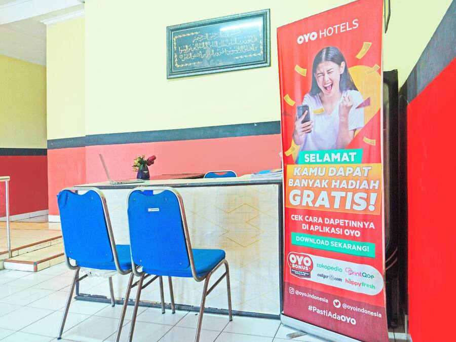 A hotel reception area with a red wall, a framed certificate, and a promotional poster for OYO Hotels.