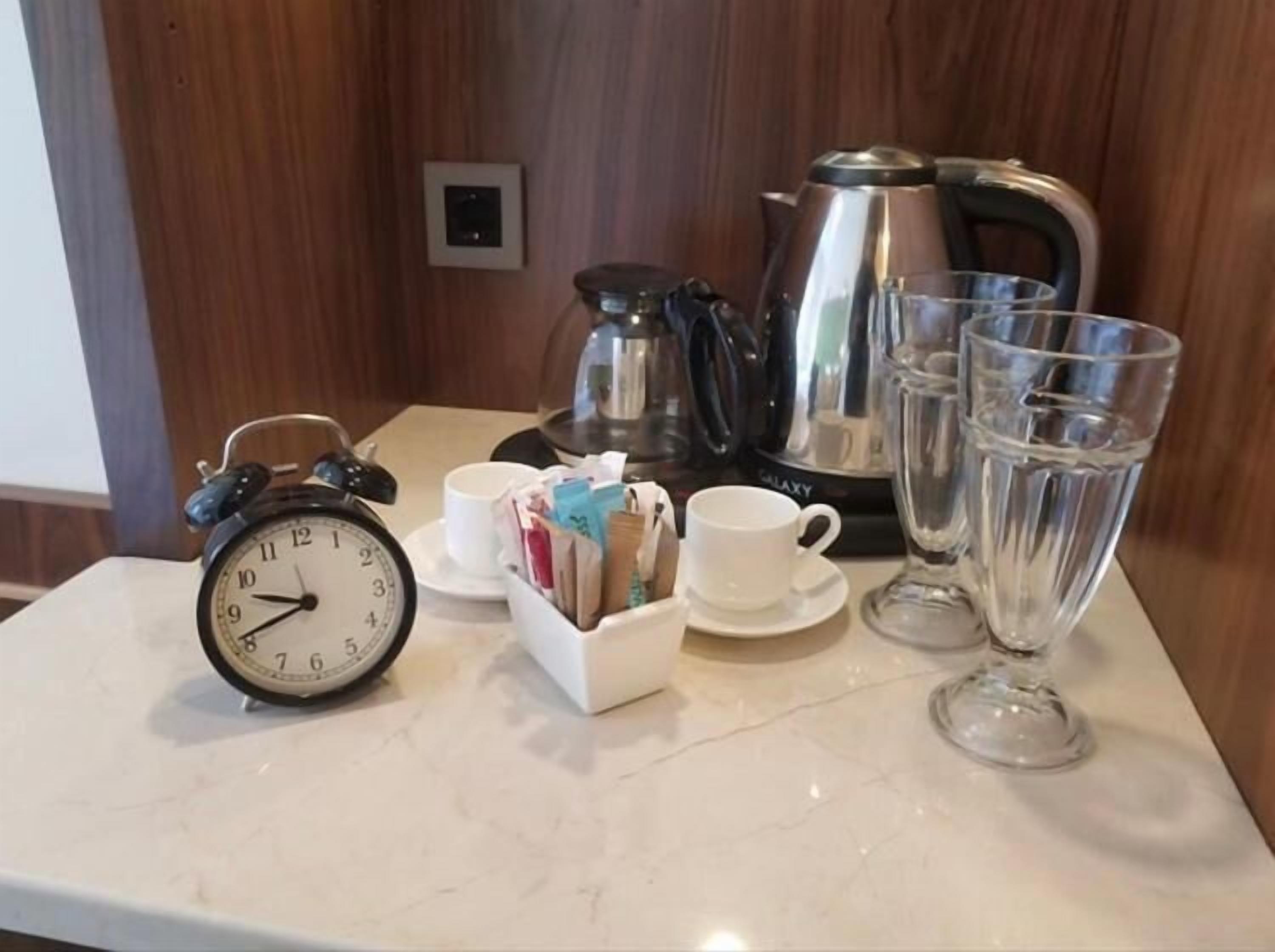A table with a clock, cups, a teapot, and glasses.