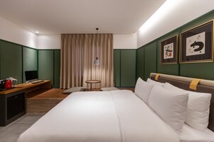 Habitación de hotel con cama, escritorio, silla, una mesita y dos cuadros enmarcados en la pared.