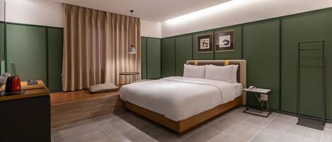 Ein modernes Hotelzimmer mit einem großen Bett, einem Nachttisch mit Lampe, einem kleinen Schreibtisch mit rotem Wasserkocher und grünen Wänden.