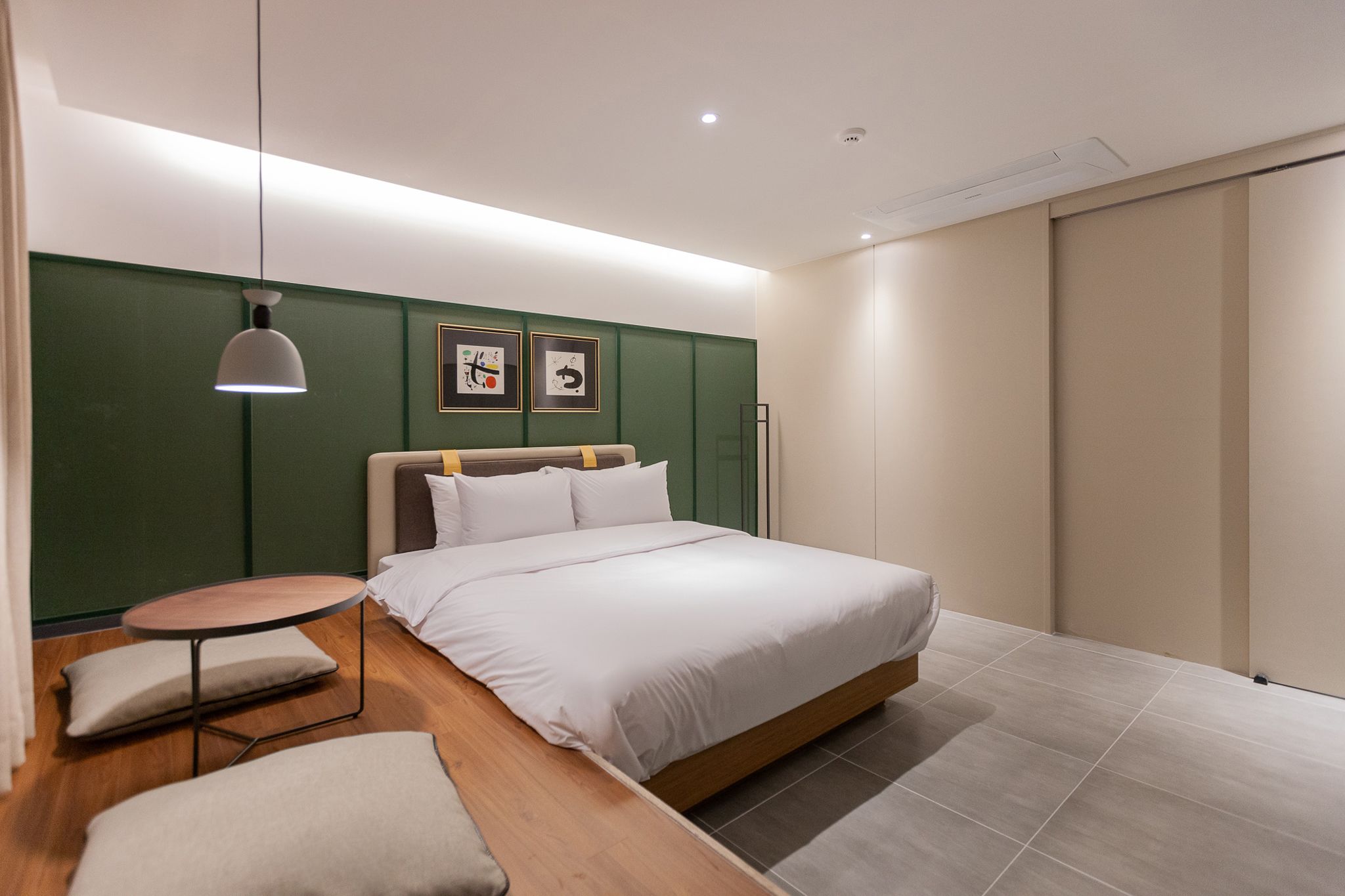A modern bedroom with a large bed, a bedside table, a hanging light, and green walls.