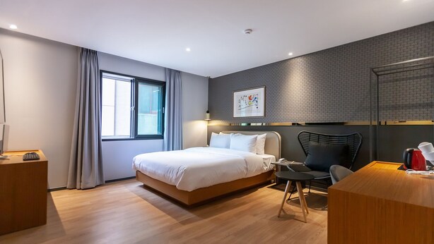 Una habitación de hotel moderna con una cama grande, un escritorio, una silla y un ventanal con cortinas.