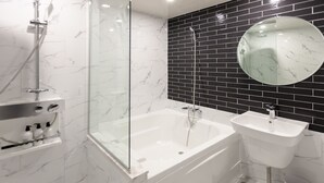 Un baño moderno con ducha de vidrio, bañera independiente y lavamanos adosado a la pared.