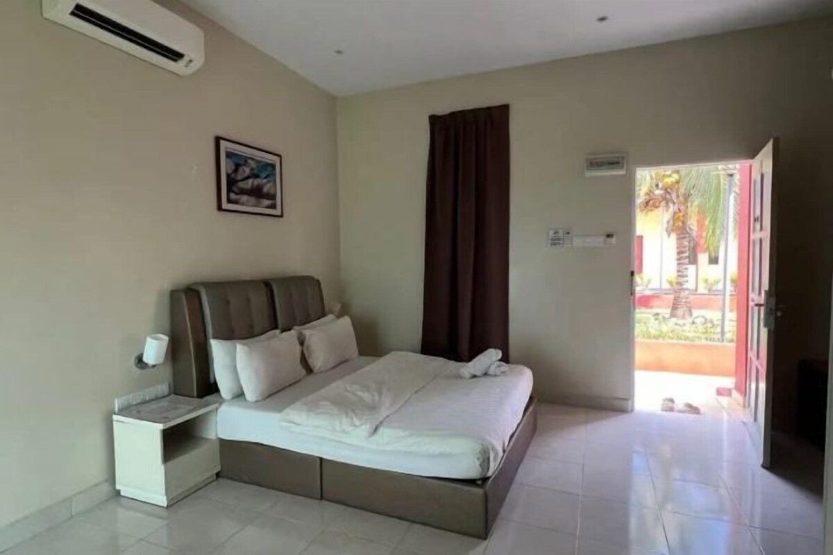 Un dormitorio con una cama, una mesita de noche, un cuadro en la pared y vistas al exterior.