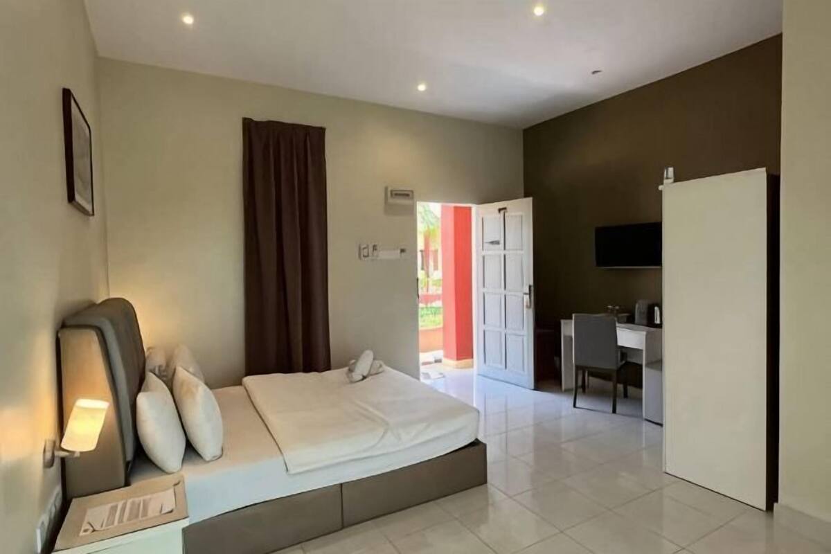 A bedroom with a bed, bedside table, lamp, and a view of a hallway.