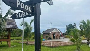 A directional signpost with 'Pool' and 'Hall' directions, a small building, and a grassy area with palm trees. - Nahdhoh Langkawi Resort (Langkawi)