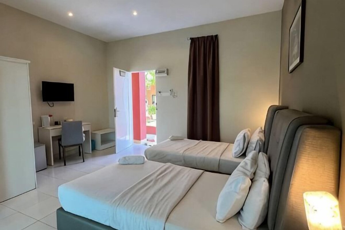 Habitación de hotel con dos camas, un escritorio, una silla, un televisor y una puerta que da a un área exterior.