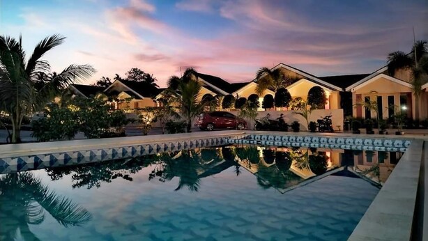 A resort with a swimming pool, palm trees, and a sunset sky. - Nahdhoh Langkawi Resort (Langkawi)