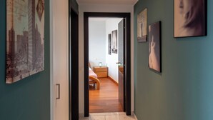 Un couloir orné d’œuvres d’art, qui mène à une chambre à coucher avec un lit et une table de chevet.