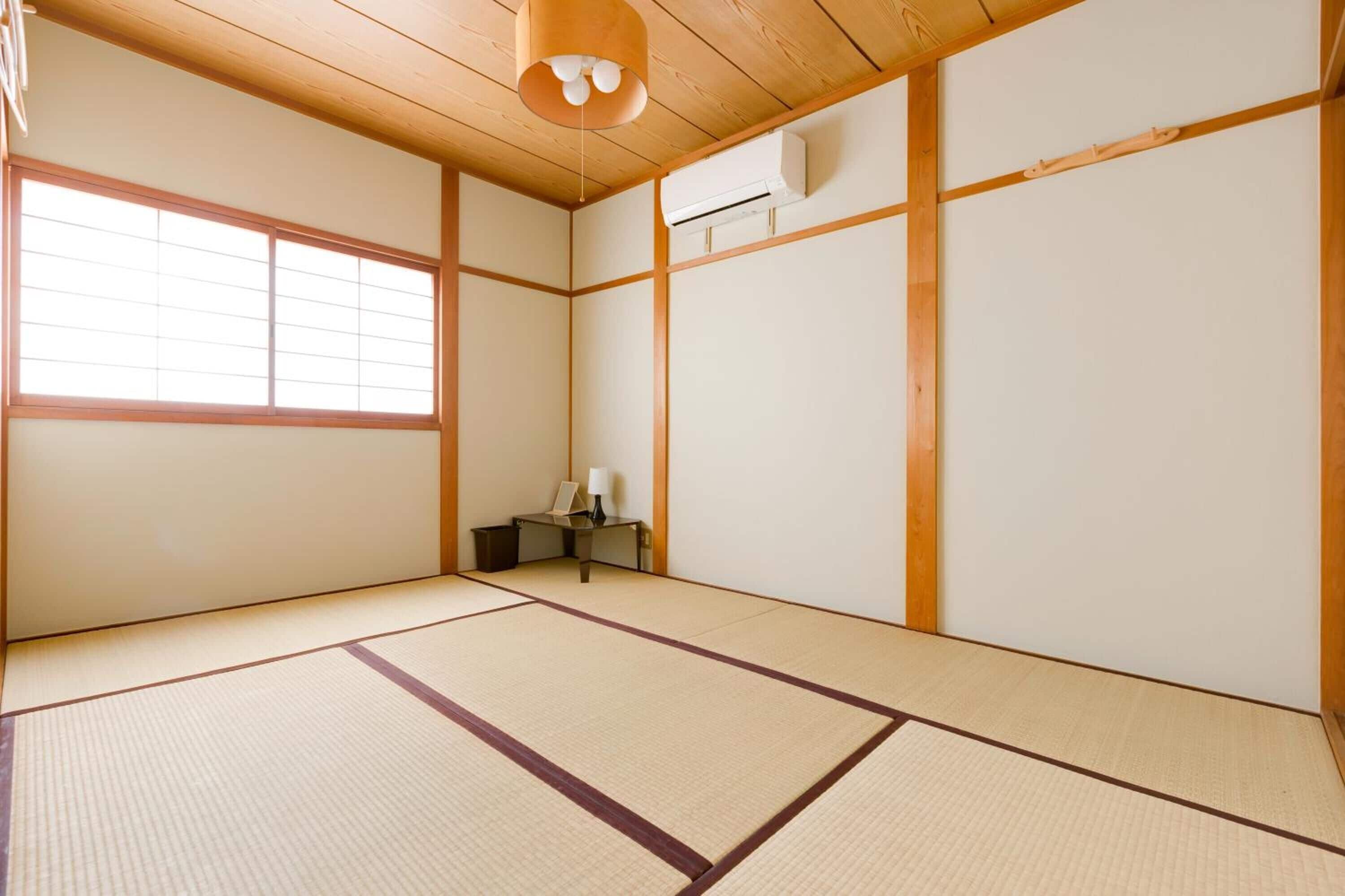 A traditional Japanese room with tatami flooring, a sliding door, a small table with a lamp, and a ceiling fan.