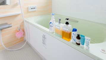 Un baño con bañera, ducha y varios artículos de aseo sobre el borde.